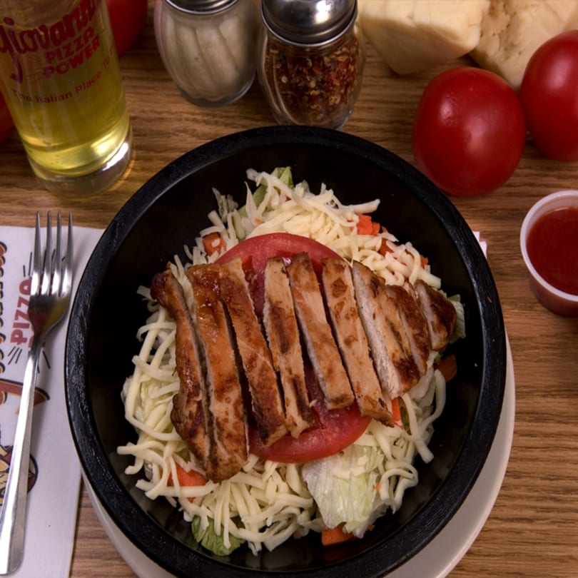 Grilled chicken salad with shredded cheese, tomatoes, and dressing on a wooden table.