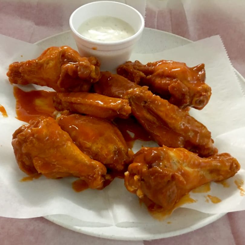A plate of buffalo wings with orange sauce and a side of ranch dressing.