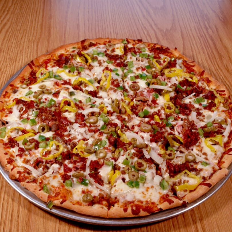 A whole pizza with cheese, sausage, green peppers, banana peppers, onions, and olives.