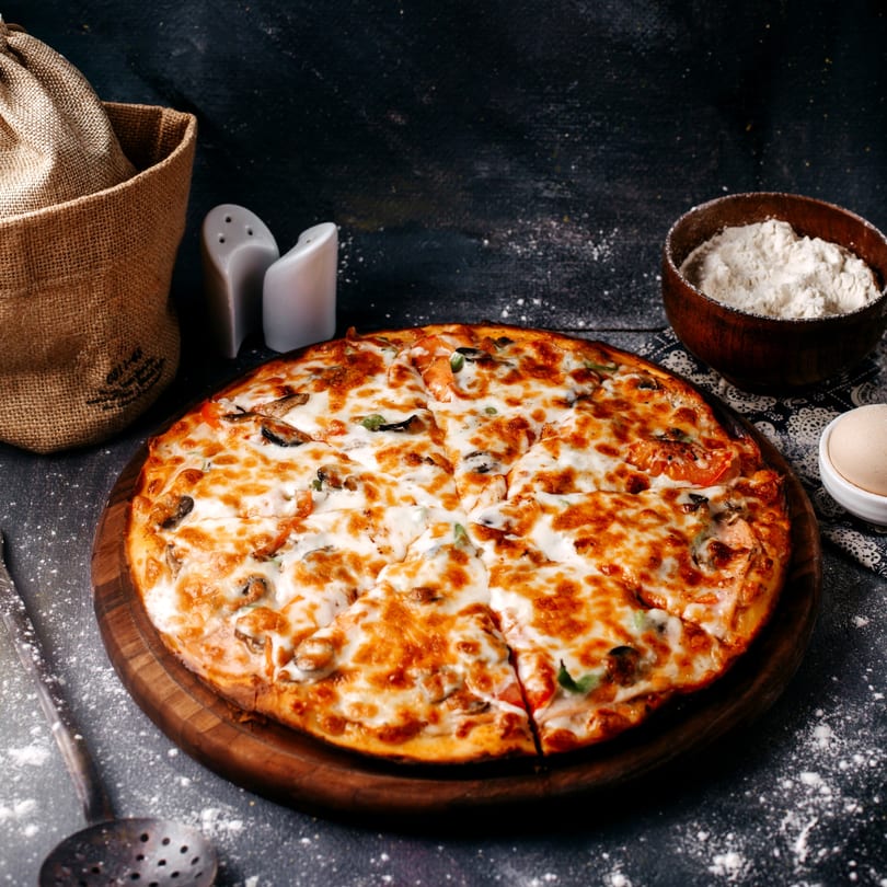 A freshly baked, sliced pizza with melted cheese and toppings on a wooden board.
