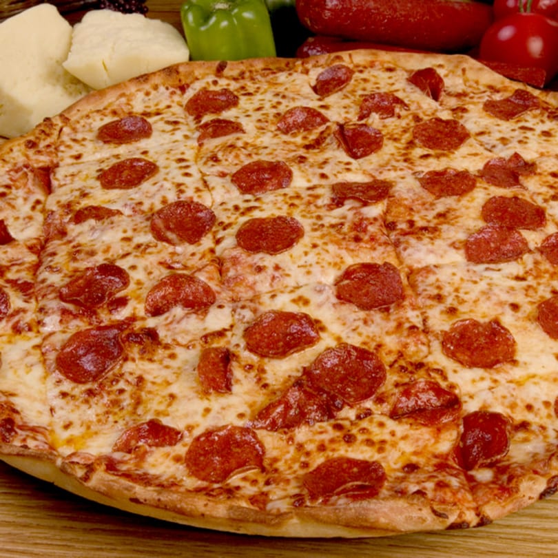 A large, round pepperoni pizza, sliced, with cheese and pepperoni, on a wooden surface.